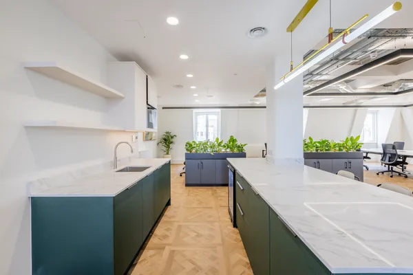 A marble-topped island over herringbone flooring in the office kitchen
