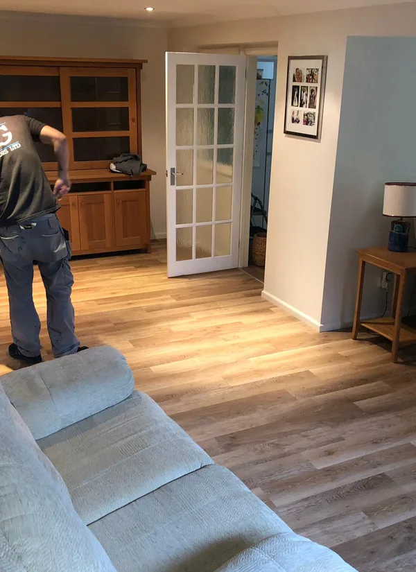 A Guild Floors fitter laying plank flooring in an occupied living room