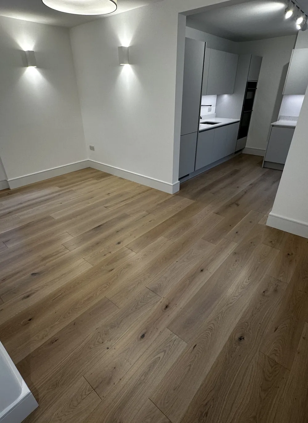 Wide-plank wood-effect flooring running through a room to the kitchen beyond