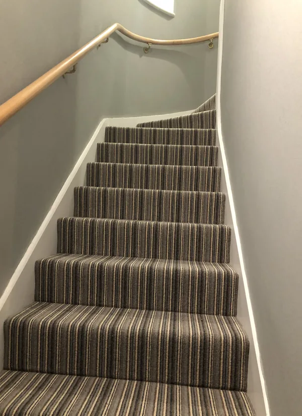 Striped stair runner fitted up a straight flight against a curved wall